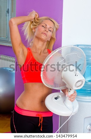 attractive woman cooling herself with electric fan in gym