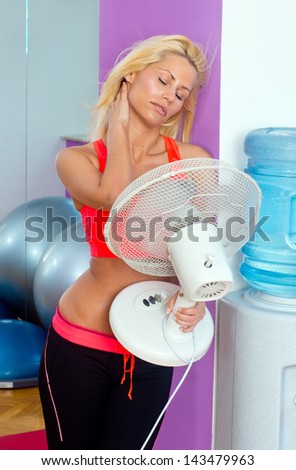 attractive woman cooling herself with electric fan in gym