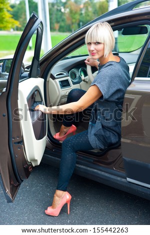 attractive blond woman in high heels sitting in her car