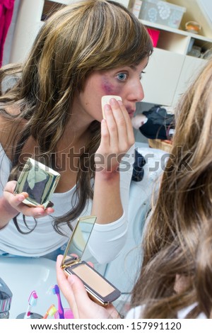 woman covering bruises with make up powder in front of the mirror