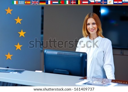 attractive woman at reception desk with european union flags behind her