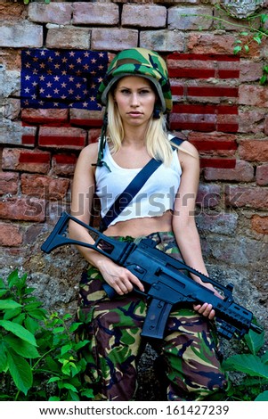 Beautiful army girl with rifle in camouflage clothes in front of wall with usa flag