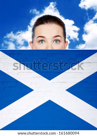 woman peeking behind wall with scotland flag