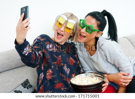 two attractive woman friends using mobile phone to make selfi picture on the sofa
