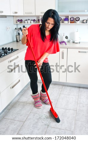 attractive brunette woman cleaning broken glass from the floor in the kitchen