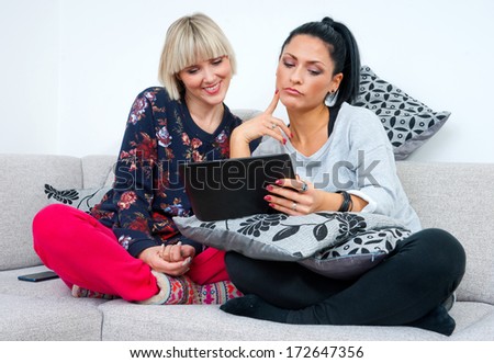 two attractive woman friends with tablet computer on the sofa