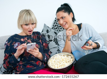 two attractive woman friends with mobile phones and popcorn on the sofa chatting