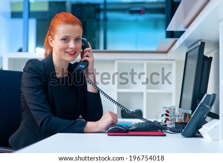 attractive modern businesswoman sitting and talking to phone in office cubicle workstation