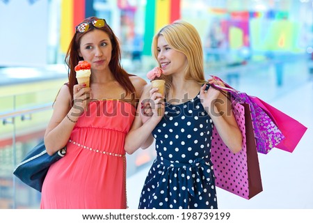 two attractive girls with ice cream and shopping bags walking