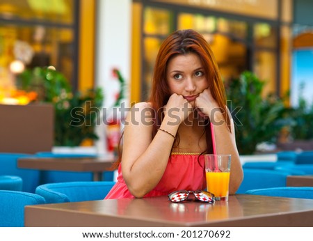 attractive sad red hair girl with orange juice sitting in bar