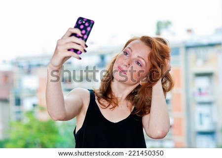 attractive red hair freckles woman makes selfie portrait with her phone outside