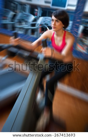 woman in gym working on bicycle machine, zoomed for dramatic effect