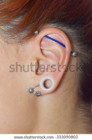 Attractive modern girl ear with plug and piercings close up