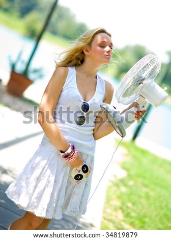 smiling girl in summer dress cooling herself with fan