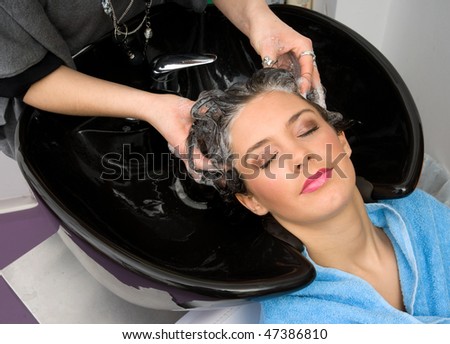 hair stylist washing woman hair with shampoo