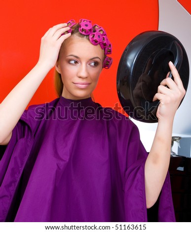 woman in salon with curlers in her hair look herself in mirror