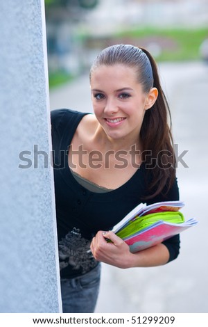 girl with school books hiding behind the wall