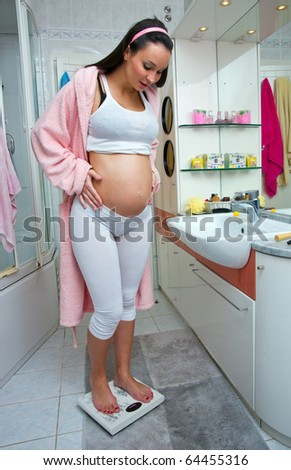 pregnant woman standing on scale weight in her bathroom