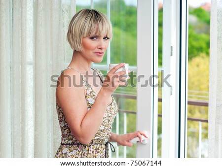 woman with morning coffee standing next to balcony window