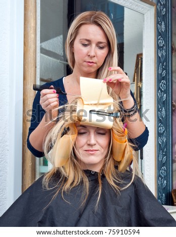 stylist putting coloring foils on woman hair in salon
