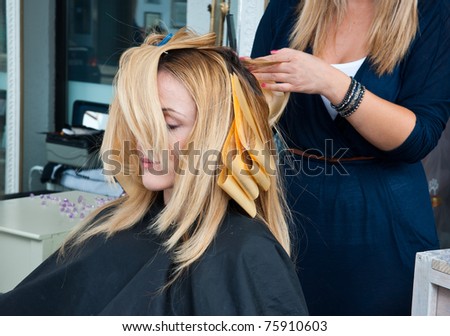 stylist putting coloring foils on woman hair in salon