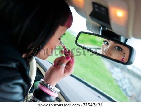 woman looking in rear view mirror and putting make up in car