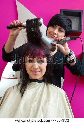 stylist with hair dryer working on teen girl in salon