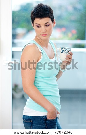 attractive sad middle age woman standing next to rainy window with coffee cup