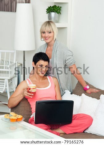 two woman friends with laptop sitting on sofa at home