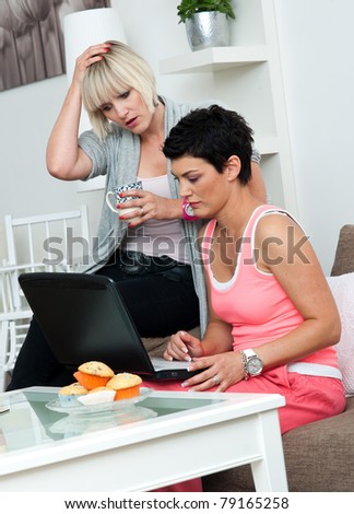 two woman friends with laptop sitting on sofa at home