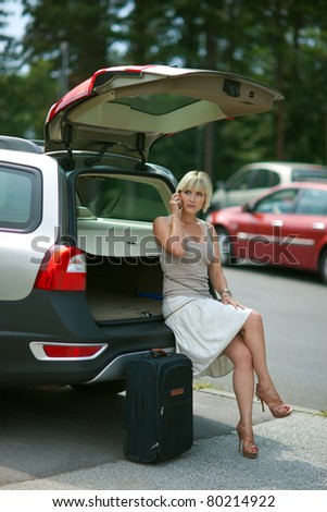 woman with baggage waiting at the car and talking to mobile phone