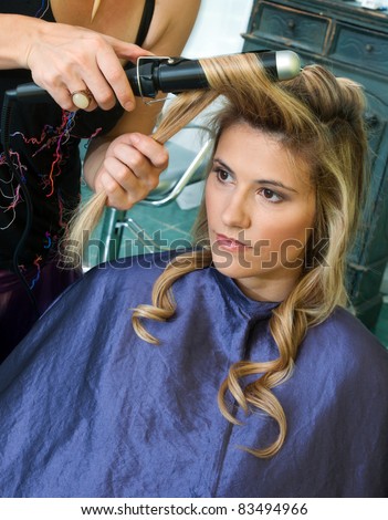 hair stylist curling woman hair in salon