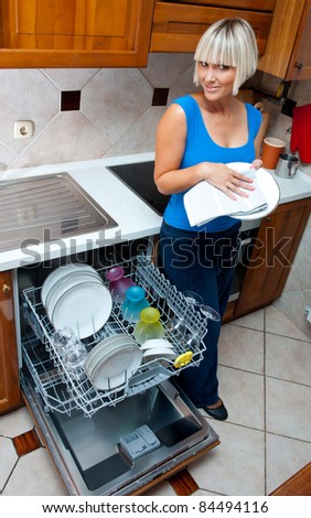 attractive housewife washing dishes in dishwasher in her home kitchen