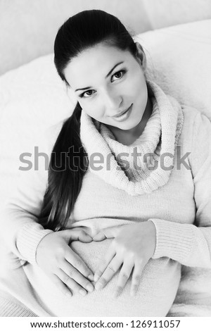 pregnant  woman with heart-shaped hands on her tummy in black and white
