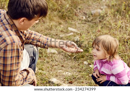 father introducing toddler daughter to the world of nature and showing little lizard