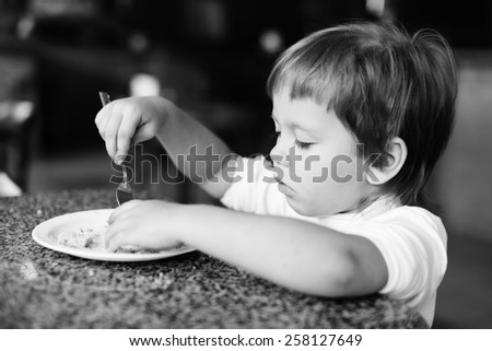 toddler girl is eating with fork in cafe