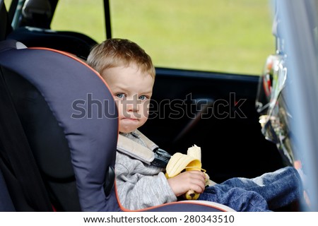 toddler boy sitting in the car seat and eating a banana