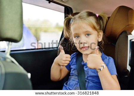 little girl sitting in car seat with thumbs up