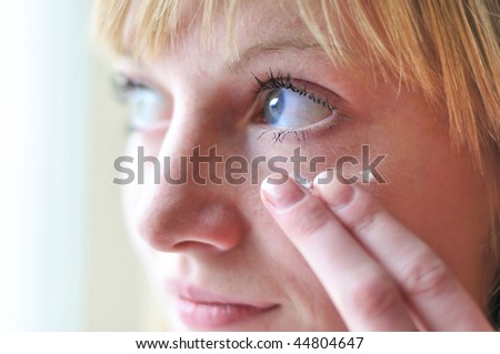 face of girl applying cosmetic cream on skin around eyes - soft focus