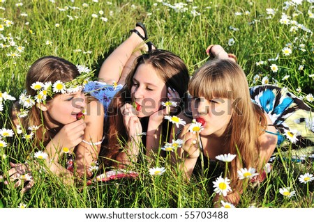 three teen girls enjoying of strawberry on the daisy field