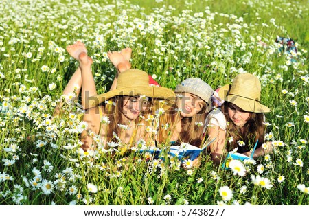 three reading barefoot girls laying on the daisy field