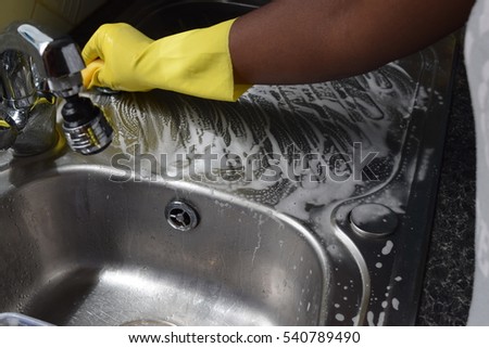 Woman with yellow gloves scrubbing the sink to clean