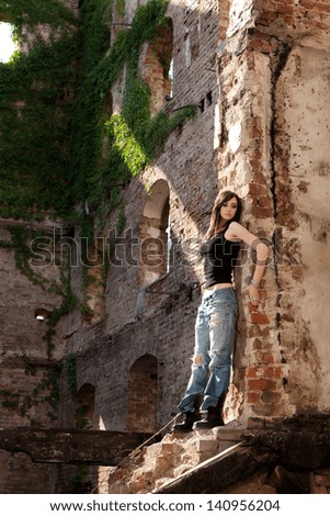 Beautiful woman with trendy style in torn jeans leaning to a brick wall.