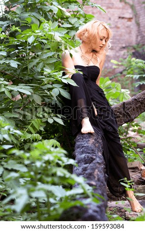 Cute sexy woman in black dress sitting playfully on a tree looking down at her foot.