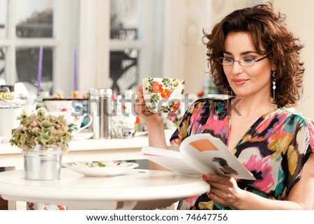 Lovely woman drinking her tea while is reading a book. See more images in the same shoot.