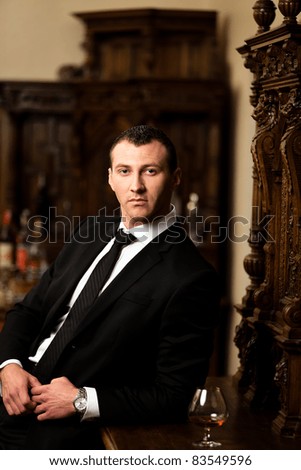 Attractive man in tuxedo having a glass of cognac. See more images from the same shoot.