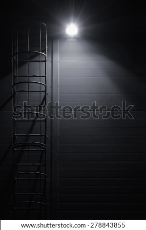 Fire emergency rescue access escape ladder stairway roof maintenance stairs night lantern lamp light shadows industrial building wall vertical closeup copy space background dark grey black