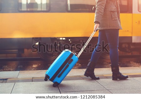 Tourist woman walking at railway station. Travel by train. Girl dragging blue luggage suitcase. Journey concept. Lifestyle, travelling, vacation. Autumn, winter travel. Woman with blue suitcase