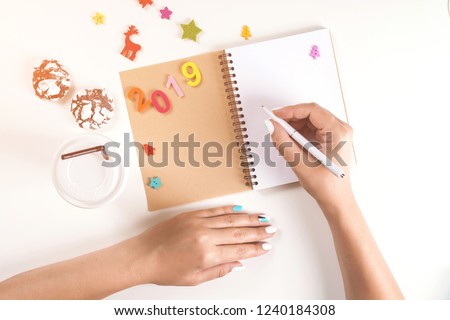 To do list for New year 2019 and Christmas. Woman hand holding pen on opened notebook. Goals plans dreams make wish list for Christmas. Winter holidays. Flat lay, top view, copy space, mock up.