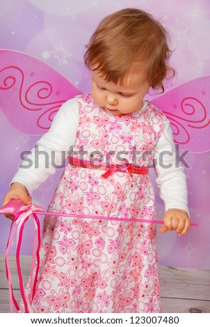adorable baby girl with fairy wings and wand on pink  background